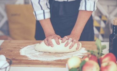 Kadın eli para kazanıyor. Un, yumurta ve diğer malzemelerle birlikte hamur, beyaz ahşap masada yatıyor. Ev yapımı pişirme işlemi.