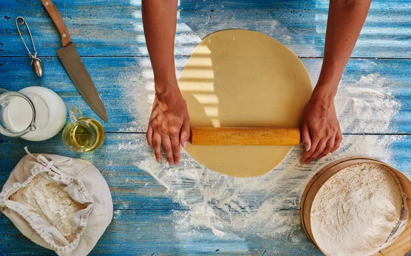 The bakery woman chef rolls the dough with a rolling pin