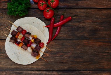 On the table is a plate with slices of bright meat on skewers