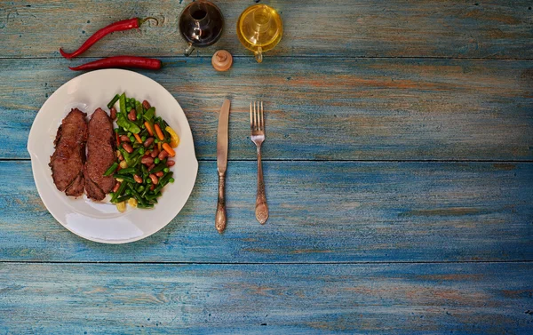 En la mesa hay un plato brillante con dos trozos de carne — Foto de Stock