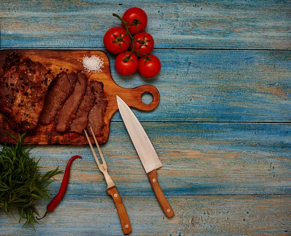 Na mesa está uma tábua de madeira na qual o chef cortou um pedaço de carne em porções. — Fotografia de Stock