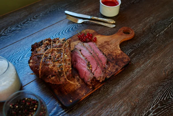 Na mesa está uma tábua de madeira na qual o chef cortou um pedaço de carne em porções. — Fotografia de Stock