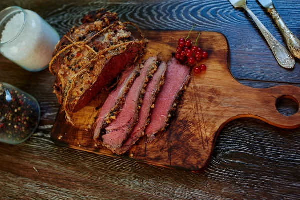 Auf dem Tisch liegt ein Holzbrett, auf dem der Koch ein Stück Fleisch in Portionen schneidet — Stockfoto