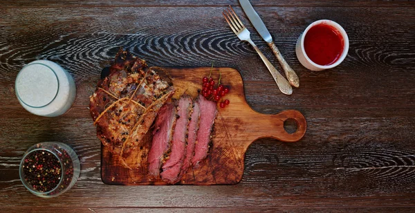 Na mesa está uma tábua de madeira na qual o chef cortou um pedaço de carne em porções. — Fotografia de Stock