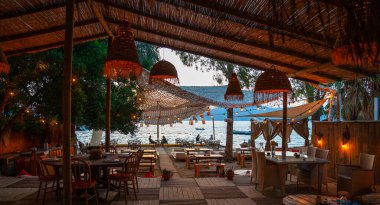 Türkiye 'de sade bir sahil restoranı. Ahşap mobilyalar, asılı fenerler ve dokuma dekorasyonlarla süslenmiş açık hava oturma alanı, deniz manzarası sunuyor..
