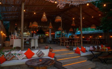 Türkiye 'de sahil kenarındaki bir restoranın rahat, loş bir köşesi. Kırsal ahşap dekorlar, rahat yastıklı koltuklar ve örülmüş fenerler davetkar bir ortam yaratıyor..