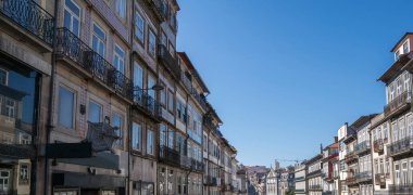 Berrak bir mavi gökyüzünün altında uzanan sakin bir sokak manzarası Porto, Portekiz 'de fayanslı ön cepheleri ve işlenmiş demir balkonları olan geleneksel Portekiz binalarını gözler önüne seriyor..