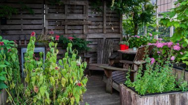 Cozy garden corner with lush greenery, wooden planters filled with herbs and flowers, a rustic wooden fence, and a shaded seating area, creating a natural and tranquil outdoor retreat.