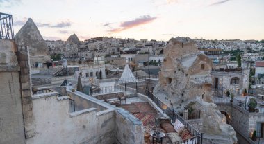 Çatı katındaki terasta bir alacakaranlık sahnesi, taştan mimarinin tarihi cazibesiyle perili baca kaya oluşumlarının doğal harikalarını harmanlıyor, batan güneşin renkleriyle boyanmış bir gökyüzünün altında.
