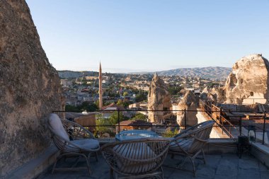 Antik kaya oluşumları tarafından çerçevelenmiş çatı terasından, alacakaranlığın yumuşak ışıltısının altında yuvarlanan tepelere karşı ince bir minaresi olan bir kasabaya bir manzara açılıyor..