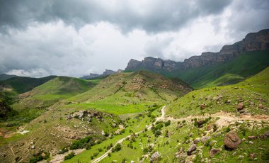 Farklı katmanlı kaya oluşumları ve yeşil yamaçları olan görkemli bir dağ sırası. Öngörülü bulutlar tepemizde belirdi, fırtınalar kopuyor, engebeli manzaranın dramatik etkilerine karşı..