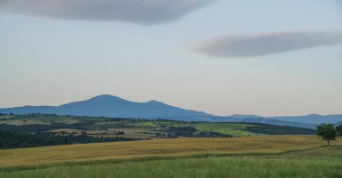 Güney Toskana 'daki Val d' Orcia manzarası. Tarlaları, yuvarlanan tepeleri, dağınık çiftlik evleri, selvi ağaçları ve sakin bir bahar akşamı Amiata Dağı 'nın silueti..