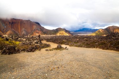 Donmuş volkanik lavlar, turuncu tepeler ve İzlanda 'nın Landmannalaugar kentindeki çok renkli dağların arasında yürüyüş yolu manzarası..