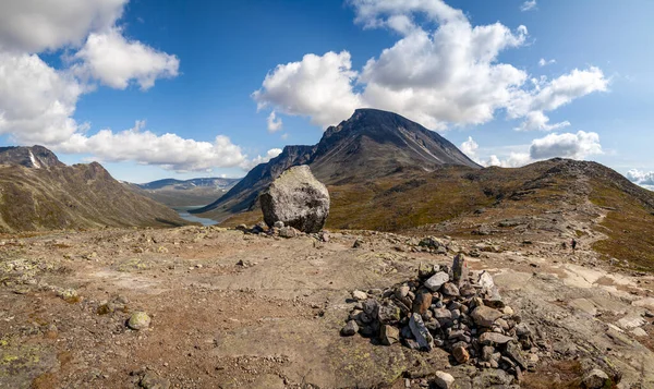 Kahverengi kayalar ve mavi yaz gökyüzünün altındaki tepeler arasında kahverengi yürüyüş patikası. Büyük taşlar ve uzak bir fiyort. Norveçte (Oppland) Auf dem Besseggen Patikası)