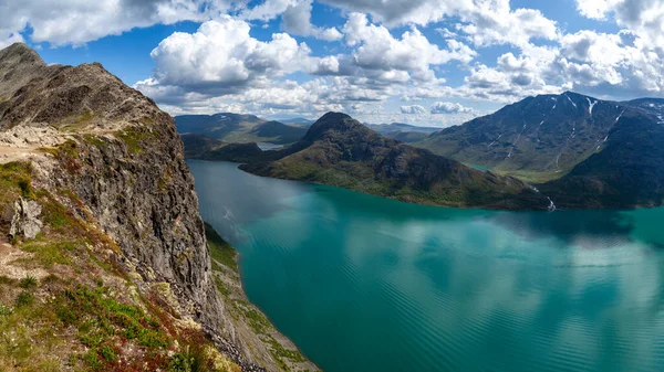 Norveç 'in Jotunheimen Ulusal Parkı' ndaki Besseggen Sırtı 'ndaki dev panorama. Ufuktaki ve mavi gökyüzünün altındaki Gjende Gölü 'nün sularındaki dağların manzaralı manzarasının uçurumundan bak. Göl yüzeyindeki bulutların yansıması.