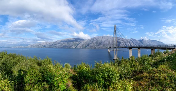 Helgeland Köprüsü 'nün mavi nehir üzerindeki panoramik manzarası ve güneşli yaz gününde Mavili gökyüzünün altındaki Seven Sisters dağ sırası. Norveç 'in Helgeland, Norveç' teki Alstahaug ve Leirfjord arasındaki en iyi köprüleri. Sandnessjoen kasabasında.