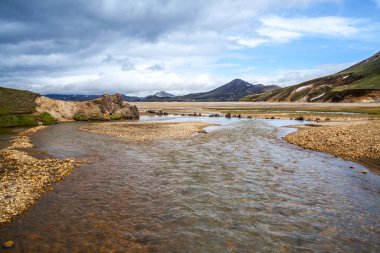 Taştan bir dağ vadisi boyunca uzanan geniş nehrin önü Landmannalaugar İzlanda
