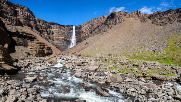 Řeka mezi kameny a vysoký vodopád v horách mezi skalami. Island. — Stock fotografie