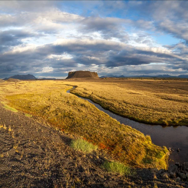 Řeka teče mezi oranžové suché trávy pole na horu na Islandu pod modrým nebem — Stock fotografie