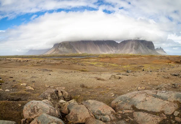 Pouštní hnědá kamenitá země před vysokou horou s vrcholkem v mracích. Island. — Stock fotografie