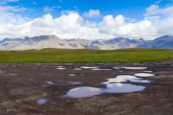 Puddle na sopečném černém písku s modrým odleskem oblohy a pohořím — Stock fotografie