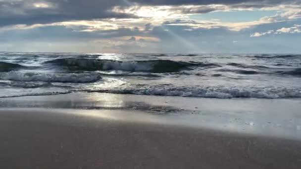 Волны катятся по мокрым песчаным пляжам при солнечном освещении и облака отражаются в воде — стоковое видео