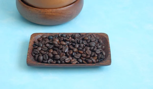 Granos de café asados en el plato de madera sobre un fondo azul — Foto de Stock