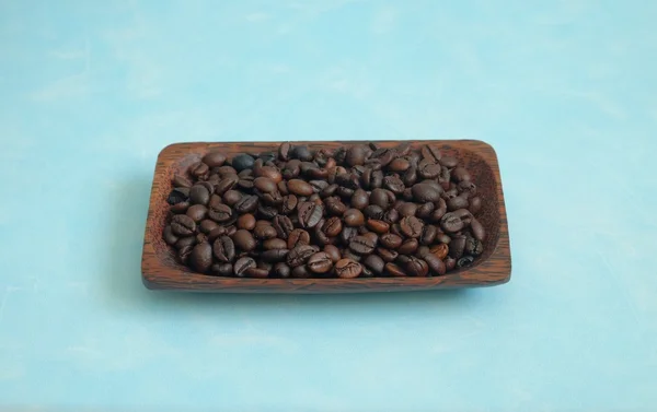 Rostade kaffebönor i träplatta på blå bakgrund — Stockfoto