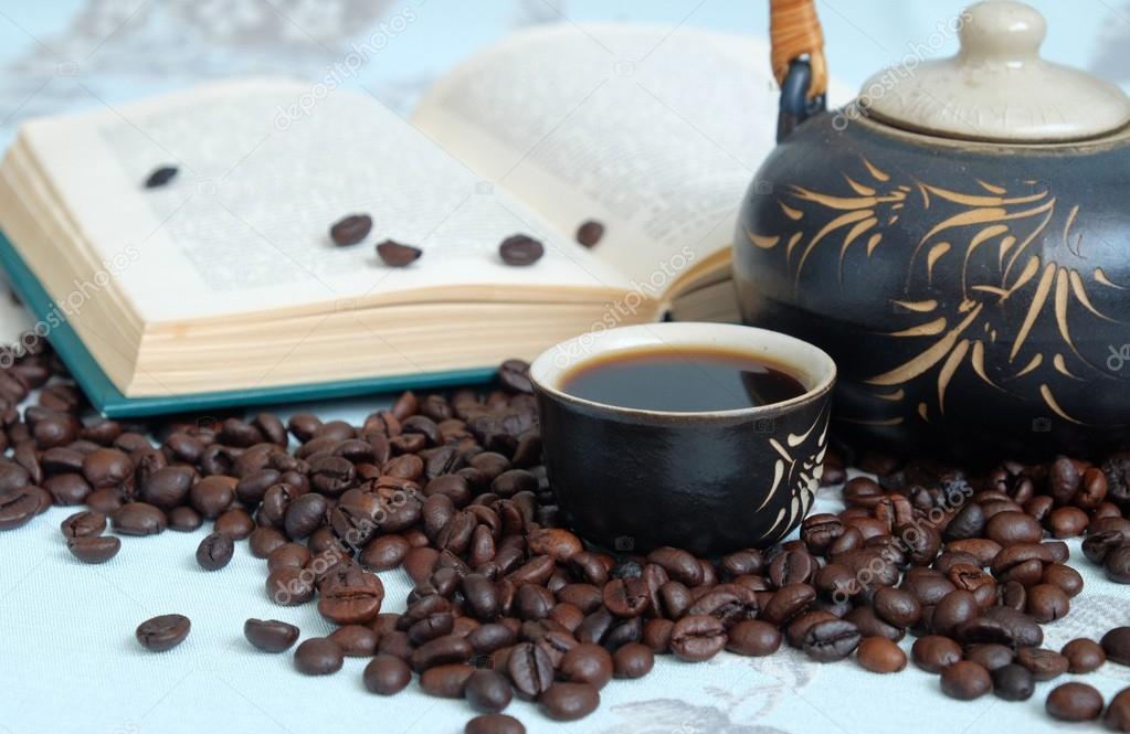 Cup of coffee, coffee beans, a teapot in the background of a closed book