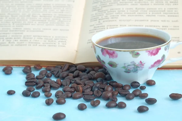 Granos de café tostados en el fondo taza de café caliente y libro abierto — Foto de Stock