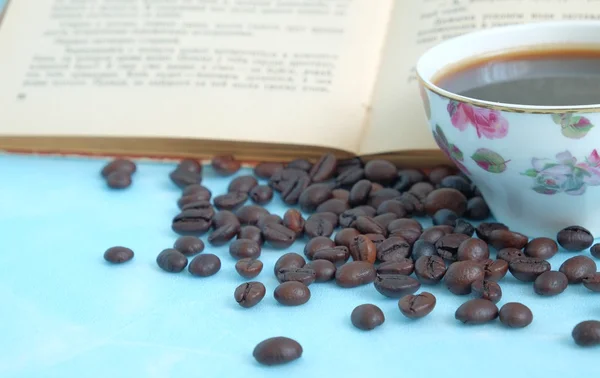 Roasted coffee beans in the background cup of hot coffee and open book — kuvapankkivalokuva