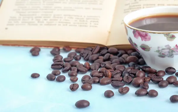 Granos tostados de café en la taza de fondo de café caliente y un libro abierto en estilo vintage — Foto de Stock