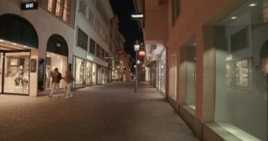 Bir şehir sokağının gece manzarası. Etrafta insanlar dolaşıyor.