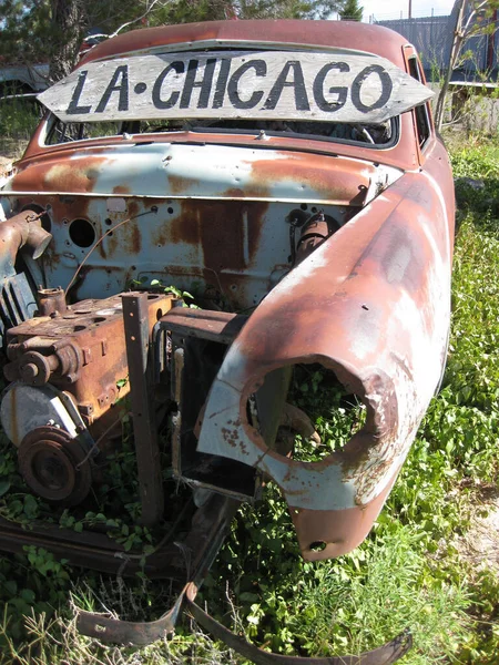 Um velho carro vintage enferrujado coberto de crescimento excessivo com um sinal dizendo LA - Chicago — Fotografia de Stock