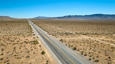 Las Vegas yakınlarındaki Nevada Çölü boyunca uzanan uzun bir otoyolun havadan görünüşü engebeli dağlar ve açık mavi gökyüzü ABD 'de açıklık ve macera hissi yaratıyor..