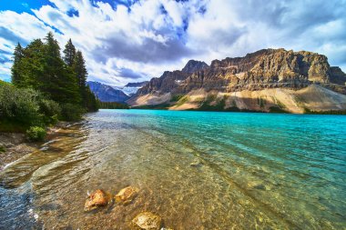 Turkuaz Bow Gölü, engebeli dağ zirveleri ve Banff Canada 'daki yemyeşil ormanların altında parıldıyor. Su sükuneti ve doğal güzelliğin nefes kesici bir manzarası yaratıyor..