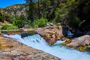 Sequoia Ulusal Parkı 'ndaki kayaların üzerinden akan Orta Çatal Kaweah Nehri' nin canlı bir görüntüsü. Kaliforniya 'nın çevresi yemyeşil ve engebeli bir yaz gökyüzü altında..