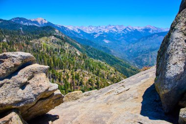 Sequoia Ulusal Parkı 'ndaki Moro Kayası' ndan geniş bir manzara, Kaliforniya engebeli granit çıkıntılarını, yemyeşil ormanları ve canlı mavi gökyüzünün altındaki Sierra Nevada sıradağlarını gözler önüne seriyor..