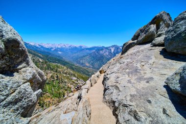 Sequoia Ulusal Parkı 'ndaki Moro Rock patikasının göz kamaştırıcı manzarası. Engebeli granit oluşumlar ve parlak mavi gökyüzü altında hareketli dağ manzaraları ilham verici macera ve keşif..
