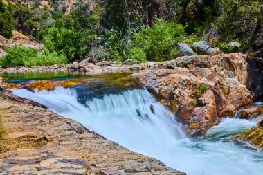 Sequoia Ulusal Parkı 'ndaki Orta Çatal Kaweah Nehri' nin canlı bir sahnesinde Kaliforniya, yoğun orman ve engebeli araziyle çevrili renkli kayaların üzerinde çağlayan sular görülüyor..