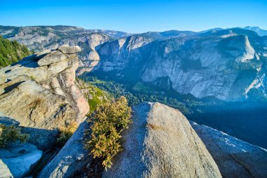 Granit, Yosemite Ulusal Parkı 'ndaki Buzul Noktası' nda yemyeşil vadi ve dramatik uçurum yüzleri masmavi gökyüzü altında ve sıcak güneş ışığı altında macera ve doğal güzelliğin ruhunu yansıtıyor..