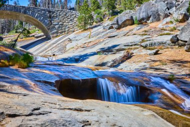 Sequoia Ulusal Parkı 'ndaki kemerlerle kaplı taş bir köprü gibi pürüzsüz bir granitin üzerinden akan nehir Mermer Çatal Kaweah Nehri' nin ve doğal manzaranın güzelliğini yakalar.