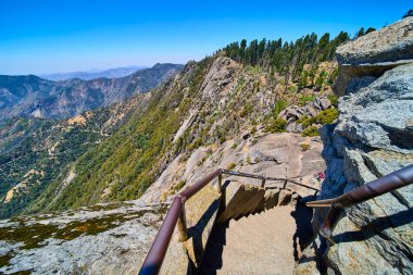 Taş basamaklar, Sequoia Ulusal Parkı 'ndaki panoramik orman ve dağ manzaralı açık bir yaz gökyüzü altında Moro Kayası' nın dik yüzüne tırmanıyor..