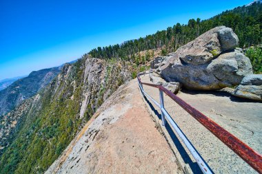 Ziyaretçiler Sequoia Ulusal Parkı 'ndaki engebeli Moro Rock patikası boyunca yürüyüş yapıyorlar. Sağlam korkuluklar, granit kayalar ve hareketli bir yaz gökyüzü altında süpüren ormansı dağ manzaraları..