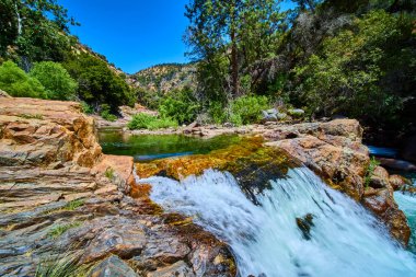 Sequoia Ulusal Parkı 'ndaki Orta Çatal Kaweah Nehri' nin el değmemiş manzarasında Kaliforniya yoğun ağaçlar ve parlak mavi gökyüzü ile çevrili renkli kayalar üzerinde akan sular yer alır..