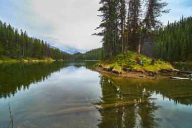 Jasper Kanada 'daki Moose Gölü' nün sakin manzarası... yemyeşil ağaçlar... sakin sularda yansıyor... küçük otlak bir ada ve uzak bir dağ manzarası..
