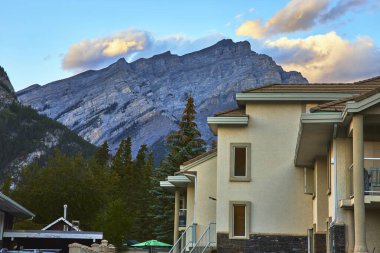 Banff Kasabası 'nda modern bir bina duruyor. Etrafı yemyeşil ağaçlarla çevrili. Kanada' da parlayan bir gökyüzünün altında dramatik dağlar yükseliyor..