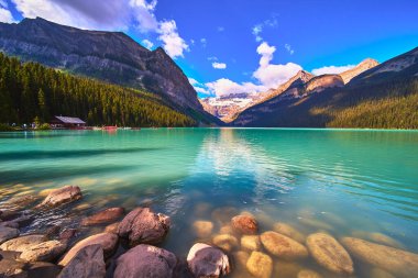 Louise Gölü 'nün sakin turkuaz suları yüksek dağlar ve açık bir yaz gününde Banff Canada' daki ormanların üzerinde yükselen buzullar gibi kayalık kıyı şeridiyle buluşur..