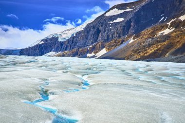Jasper Canada 'daki çarpıcı Athabasca Buzulu engebeli dağ kayalıklarının yanında canlı mavi buz yarıkları ve çarpıcı ve el değmemiş doğal bir manzara yaratan parlak bir gökyüzü sergiliyor..