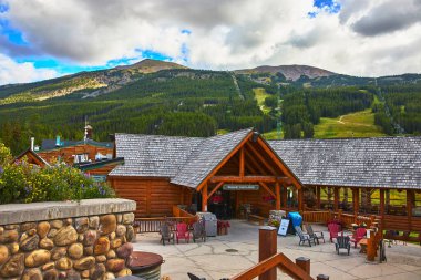 Banff Canada 'daki yemyeşil dağ yamaçlarının eteklerinde oturmakta olan kır evi bulutlar gökyüzünde süzülürken ve kır çiçekleri taş duvarların yanında çiçek açarken karşılayıcı bir dağ inzivası yaratıyor..